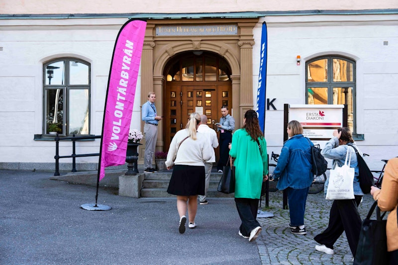Besökare går in till ett volontärevent hos Ersta Diakoni med Volontärbyrån-flaggor vid entren.